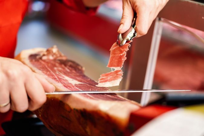 Close up of female hands in butcher shop cutting ham