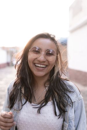 A young Hispanic woman with sunglasses is smiling posing in the street during the sunset