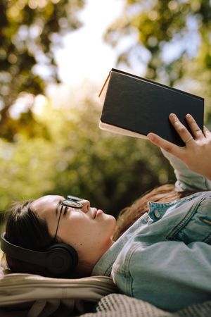 Close up of a young woman lying on ground and reading a book wearing headphones