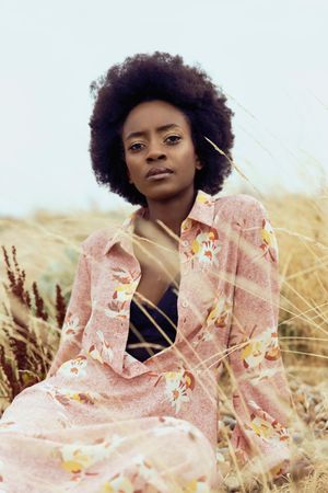 Woman in pink floral robe sitting on brown grass field
