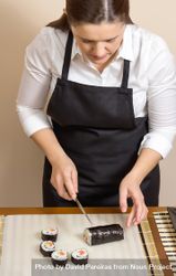 Female chef in apron cutting sushi rolls on table, vertical 0JmeNb