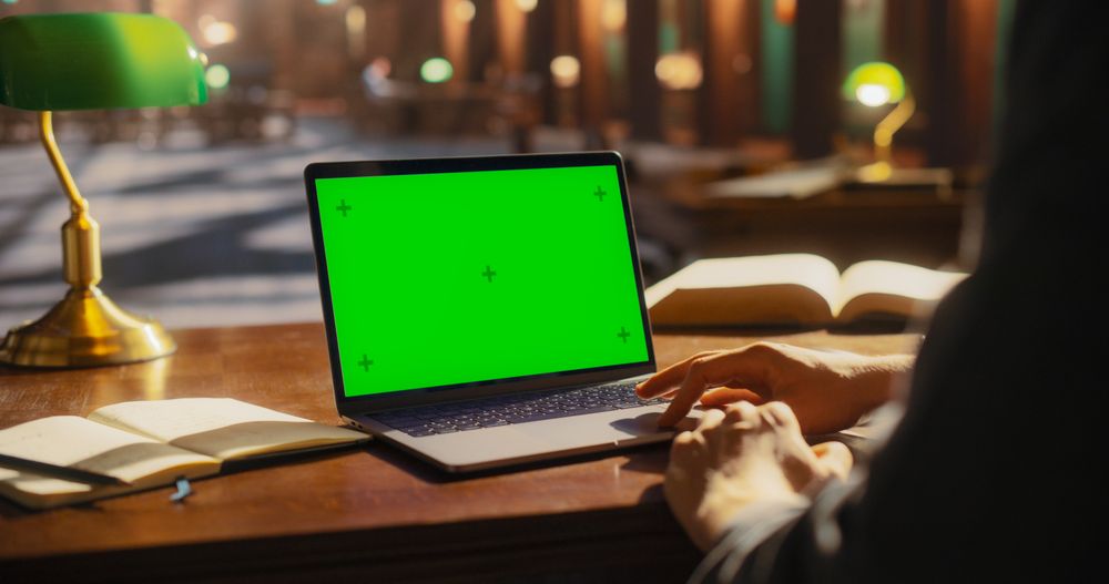 Engaged Student Working on a Laptop with Green Screen in a Classic Library