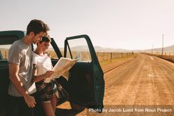 Young couple standing beside classic truck on open road holding map while on road trip 56W2Y4