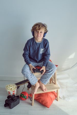 Unhappy boy playing game with controller and headphones
