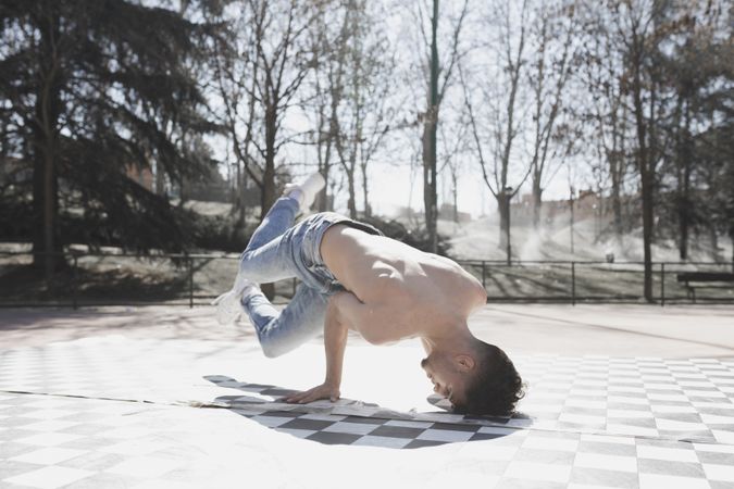 Shirtless man dancing break dance in park