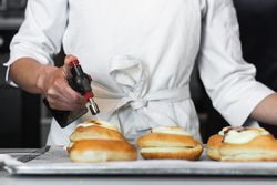 Crop cook burning cream on dessert with gas burner in bakery