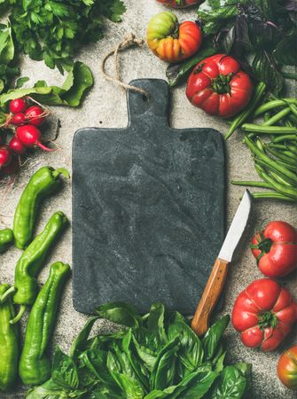 Fresh vegetables arranged with dark cutting board and knife in center, vertical composition