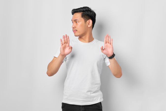 Asian male in grey studio gesturing “no” with both hands facing forward