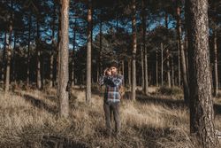Confident photographer taking picture with camera in sunny forest