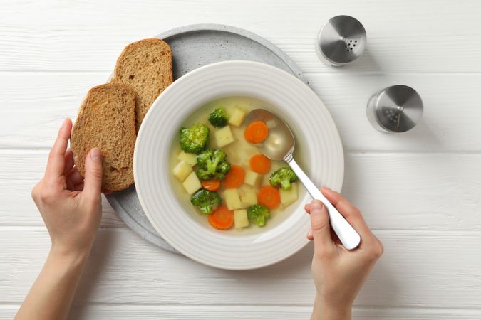 Top view person’s hands with spoon in vegetable soup