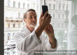 Grey haired man with beard taking a selfie out the hotel window bYXkg4