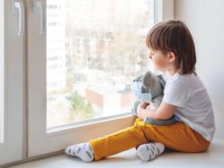 Toddler boy sits with teddy bear in medical mask