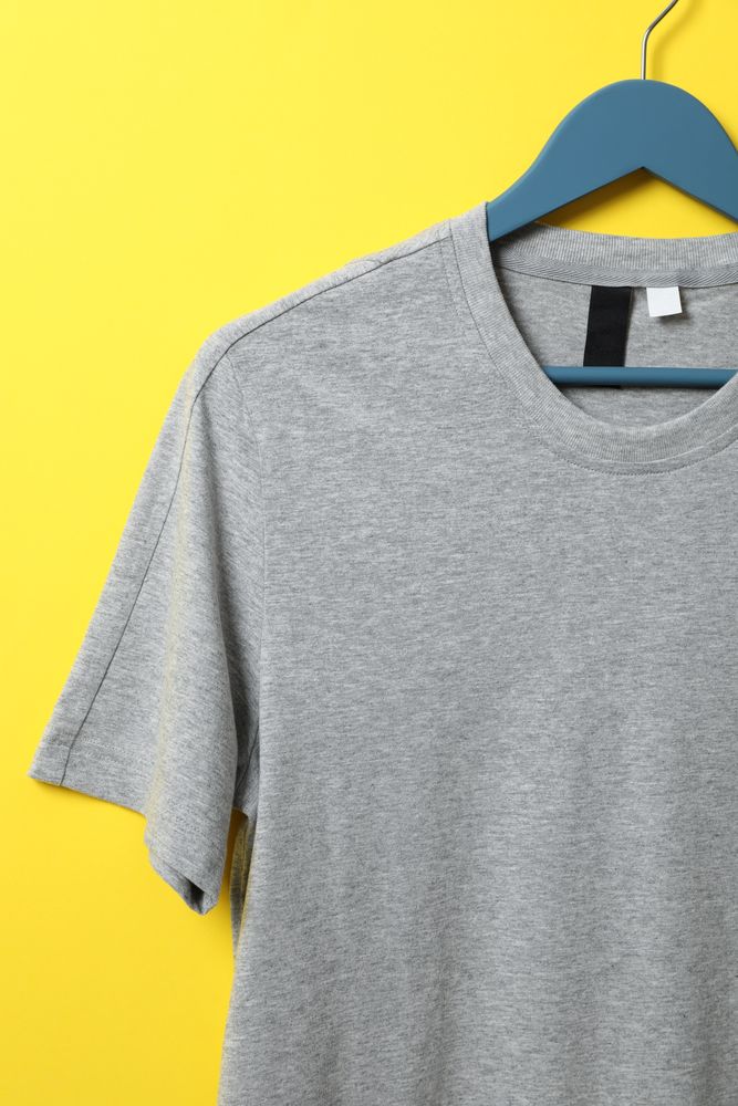 Hanger with blank gray t-shirt on yellow background, space for text