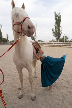 woman in skirt leaning on horse side while dancing at paddock