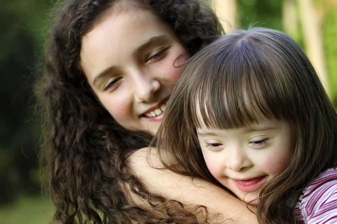 Close up portrait of two adorable sisters snuggling together at the park