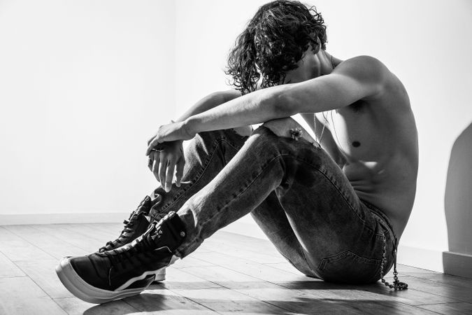 Grayscale of young topless man hugging his knees