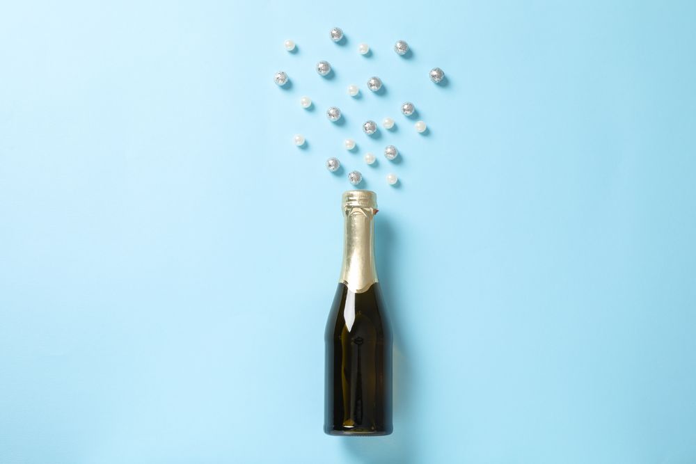 Champagne bottle and glitter on blue background, space for text