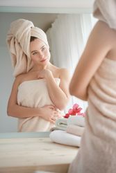 Confident woman in towel looking at reflection in mirror