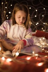 Girl reading book in bedroom decorated with Christmas lights