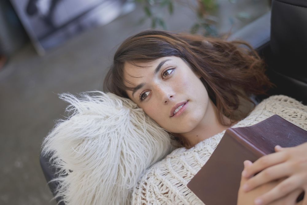 Portrait of woman lying on sofa with book on her chest