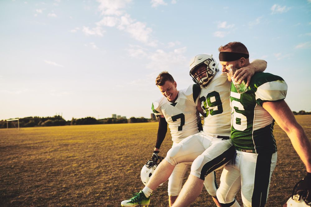Two footballers carrying an injured teammate off the field