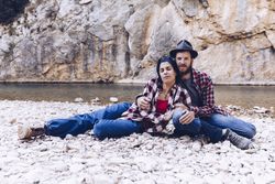 Positive woman and man resting on stone shore near river