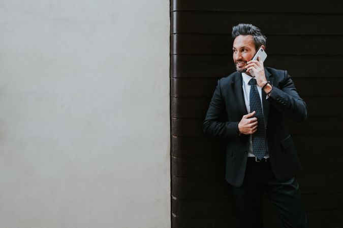 Adult stylish man in costume talking on smartphone near wall