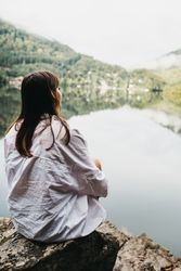 Woman sitting on rock near lake and mountains
