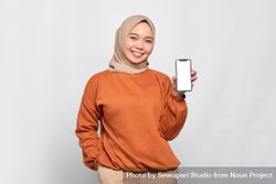 Happy Muslim woman smiling with hand in pocket presenting smart phone with mock up screen 5le9e4