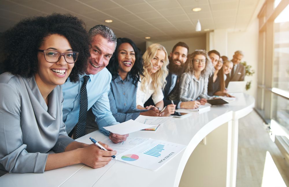 Multi-ethnic group of people in office attire standing and smiling in a row at work