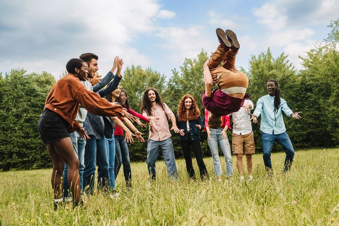 A group of multi-ethnic friends gathered in a circle while a man does a somersault