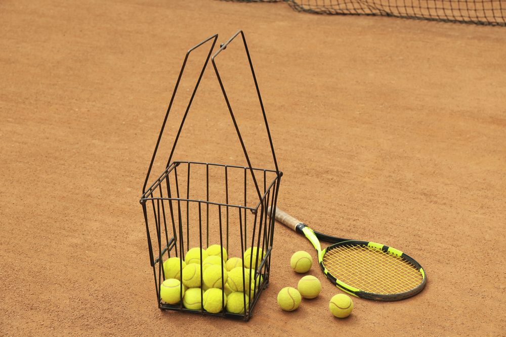 Racket and basket with balls on clay court