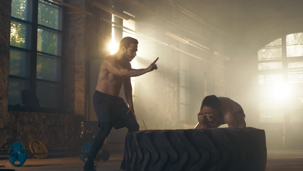 Fit Athletic Woman Lifts Tire Under Supervision of Her  Trainer