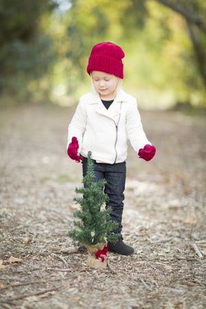 Girl In Red Mittens and Cap Near Small Christmas Tree
