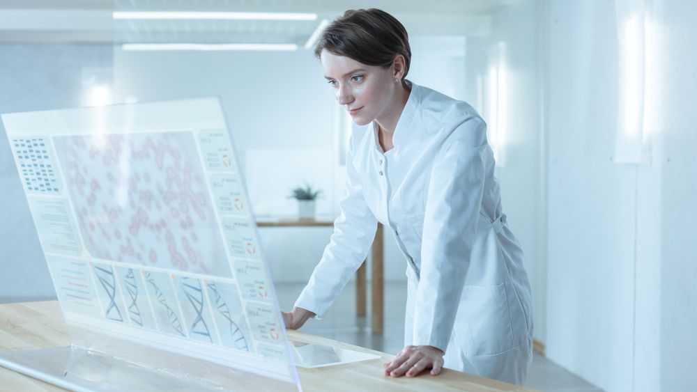 In the Futuristic Laboratory Female Scientists Working on Deciphering Sequenced Human DNA on the Transparent Display Computer.