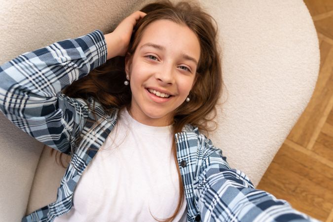 Girl lying on sofa taking happy selfie at home.