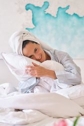 Dreamy female hugging pillows on bed at home