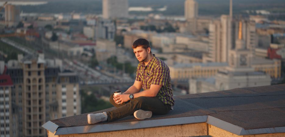 Male, lost in thought sitting on roof drinking coffee