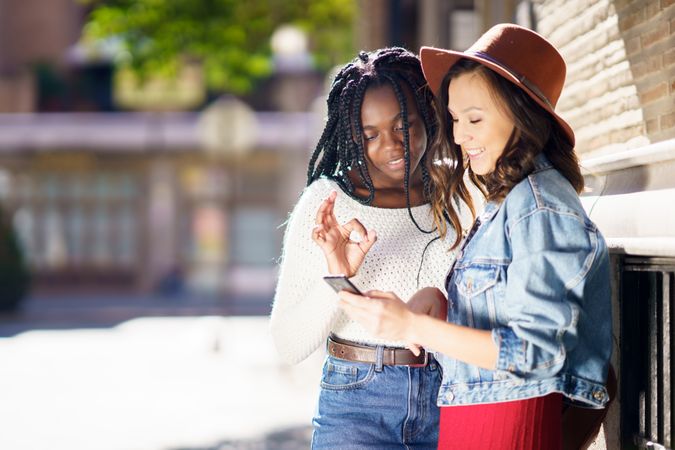 Female friends both intently looking down at a cell phone