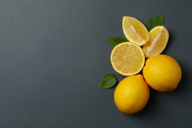 Fresh lemons with leaves on dark background, top view. Ripe fruit