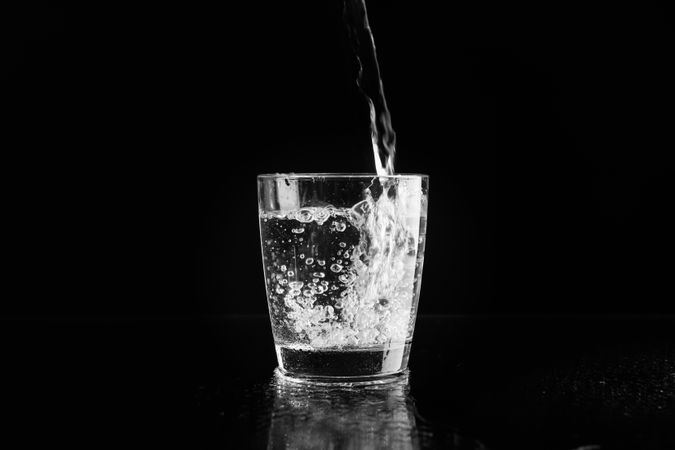 Glass of water being poured in dark room