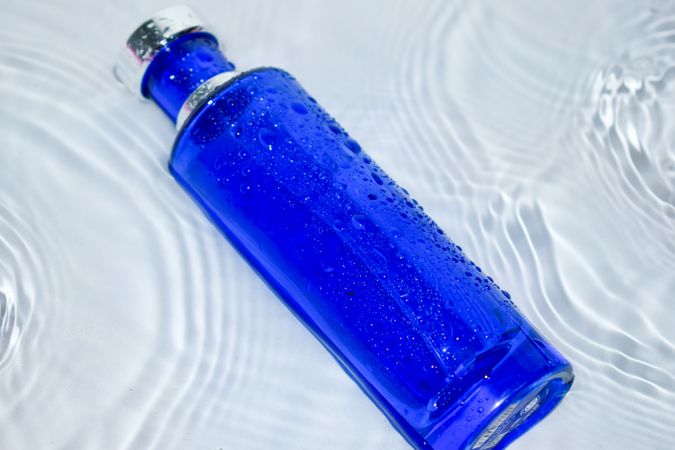 Blue perfume bottle on light background with water rippling around it