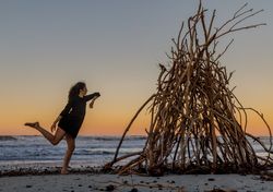 Young woman dancing on shore near water and wooden twigs placed for campfire