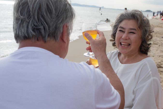 Older Asian couple relaxing on the beach and toasting with wine