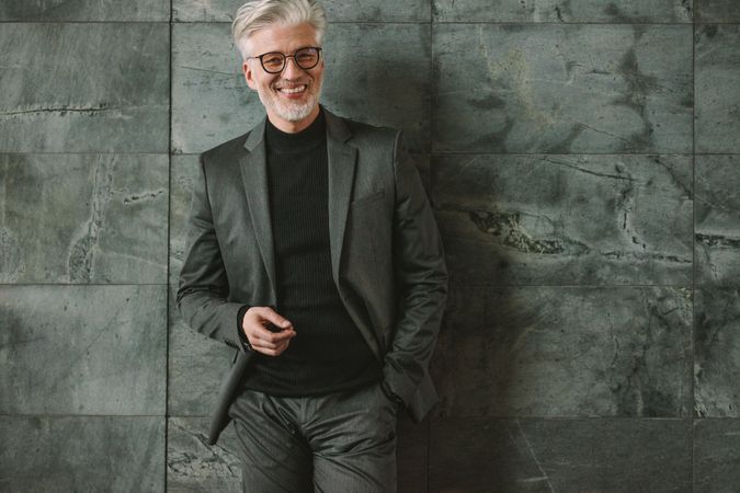 Portrait of good looking mature businessman standing relaxed on grey wall