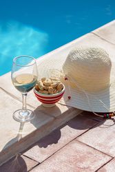Glass of wine, peanuts, and a sun hat by the swimming pool on a sunny summer day
