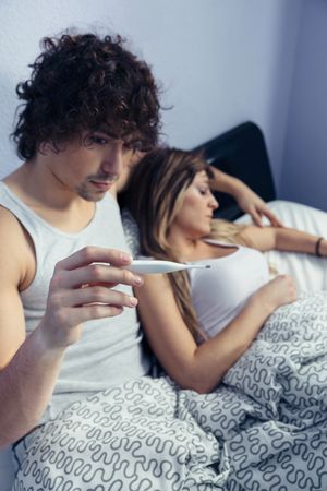 Man looking at temperature of sick woman in bed