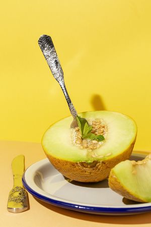 Sliced small melon on plate with spoon and fork