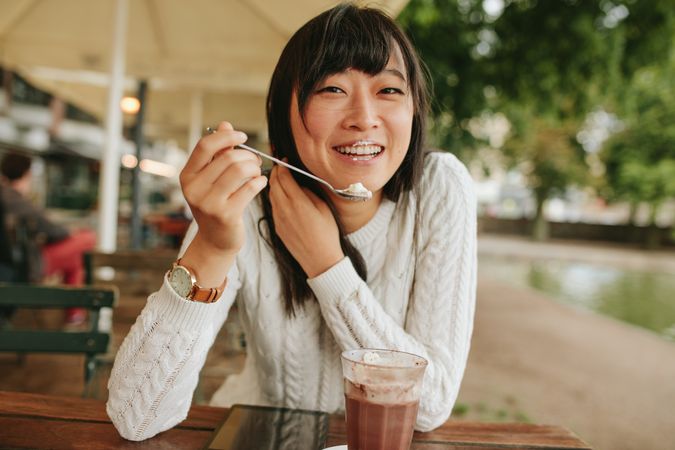 Shot of happy young woman at outdoor cafe eating cold dessert of ice cream
