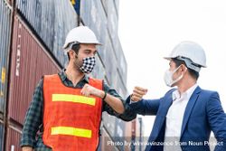 Construction site worker and foreman wearing hygiene face mask elbow bump greeting bE6Nl0